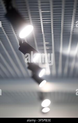 Modern track lighting system installed on a bright metallic grid ceiling features multiple glowing spotlights arranged in a linear row to provide illu Stock Photo