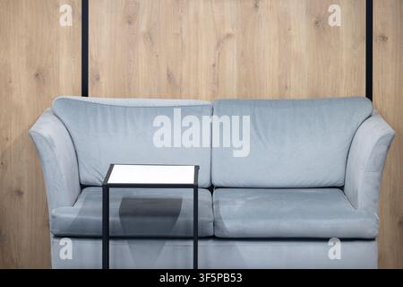 Modern light blue velvet sofa with a small white side table placed against a light natural wooden wall panel background elegant black vertical accents Stock Photo