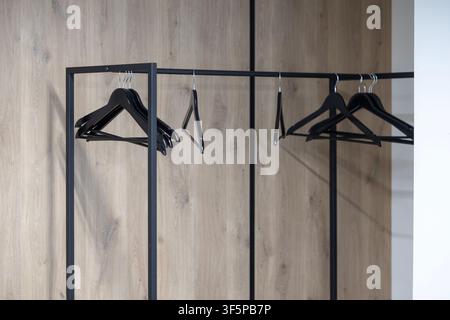 Modern wardrobe rack with black wooden hangers arranged against a light brown textured wood grain wall surface providing a minimalist storage solution Stock Photo