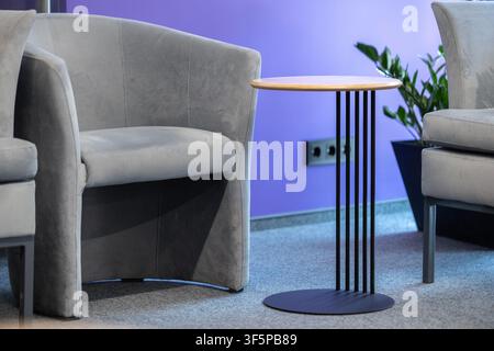 Modern interior design comfortable grey upholstered chairs positioned around a small round wooden table with metallic legs against a vibrant purple wa Stock Photo