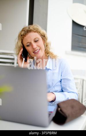 Woman using laptop and smartphone for remote work outdoors Stock Photo