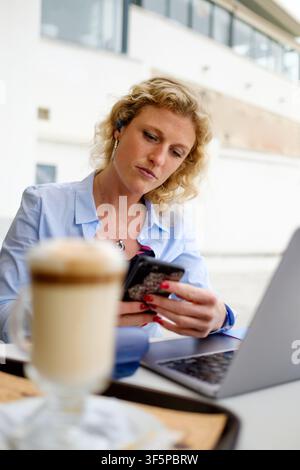 Woman focusing on her smartphone while working remotely at an outdoor cafe Stock Photo