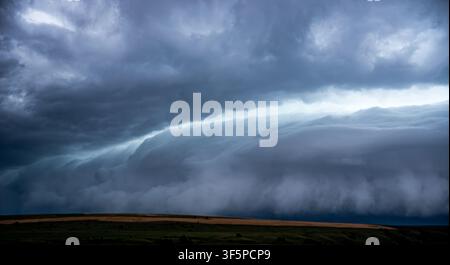 Dramatic landscape featuring a massive shelf cloud of a supercell thunderstorm moving over a rural road and countryside fields, capturing the powerful Stock Photo