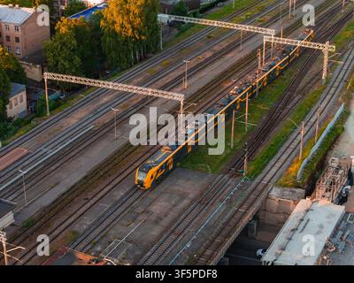 Yellow Passenger Train on the Tracks in Riga at Sunset Stock Photo