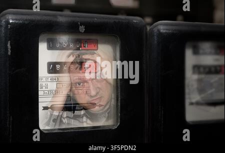 Electrical meter with reflection of shocked customer reading electricity consumption. Closeup of stressed man checking electric power measuring device. Stock Photo