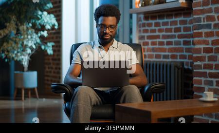 Happy African American business man smiling in room typing laptop device smile chatting with computer businessman guy male in home office employer Stock Photo