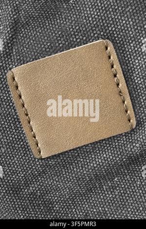 Blank yellow leather patch stitched on black fabric background closeup Stock Photo
