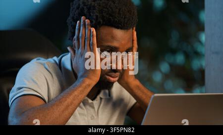 Tired stressed African American business man holding head looking at laptop at night office ethnic male businessman guy executive professional feeling Stock Photo
