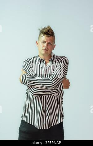 Luke Wright poses with his arms crossed in front of a light backdrop. He wears a black and white striped shirt and appears focused. The setting looks Stock Photo