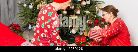 A couple aged 52 shares a joyful moment together on Christmas Day. They are near a decorated Christmas tree, opening gifts and enjoying the holiday atmosphere Stock Photo