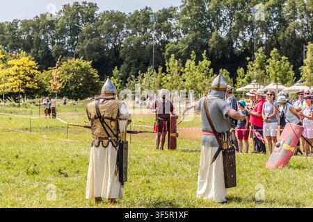 Two archers in white tunics stand ready with bow and arrow, their quivers hanging from broad belts. A legionary with a red shield waits in the background on the meadow at the Landesgartenschau (LAGA) garden show in Neuss, Germany. Stock Photo