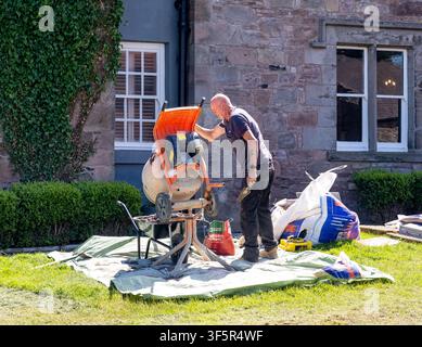 General builder mixing concrete in a small cement mixer, on-site construction work, hands-on manual labour, industrial tools, and practical building p Stock Photo