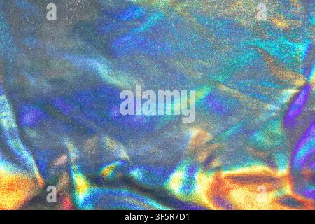Shimmering holographic foil texture with iridescent rainbow highlights, metallic sheen and abstract reflective surface detail. Stock Photo