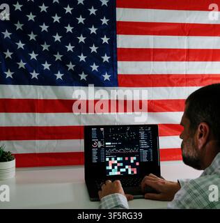 Man working on laptop displaying surveillance tracking dashboard in front of American flag, representing digital privacy and Fourth Amendment rights Stock Photo