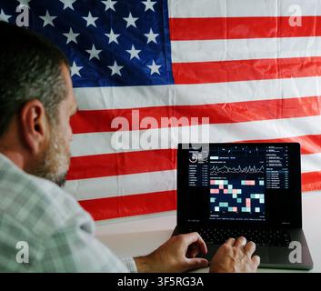 Man working on laptop displaying surveillance tracking dashboard in front of American flag, representing digital privacy and Fourth Amendment rights Stock Photo