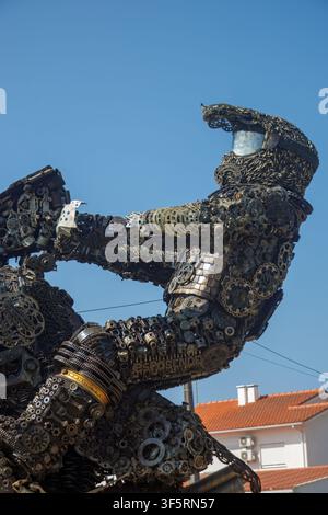 Scrap metal sculpture of a motorcycle rider in full gear, built from recycled auto and bike parts against blue sky. Stock Photo