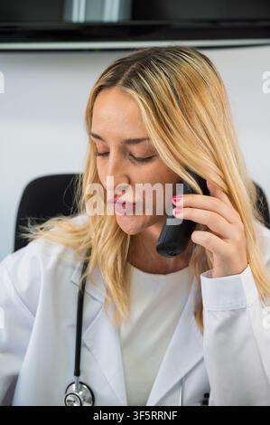 Female doctor communicating on a phone call while wearing a stethoscope and white lab coat Stock Photo