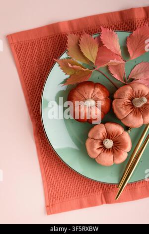 Three decorative velvet pumpkins are arranged on a mint green plate with a sprig of colorful autumn leaves and golden chopsticks, signifying the fall Stock Photo