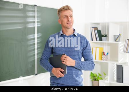 Smiling teacher with laptop near chalkboard in classroom Stock Photo