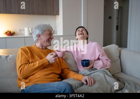 Cheerful happy senior married couple sitting resting on couch at home joking and laughing together. Stock Photo