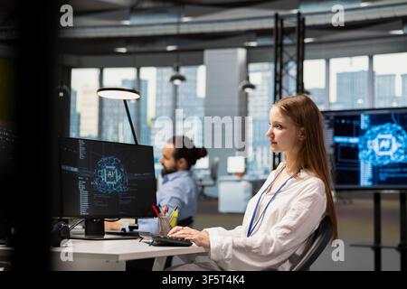 Female developer in modern office leveraging AI tools to automate routine coding tasks. Young programmer using artificial intelligence to accelerate software feature development Stock Photo