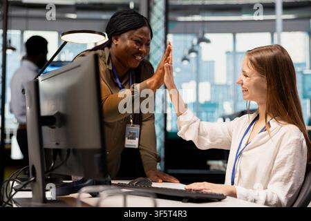 Jolly manager praising code written by female technician, doing high five. Happy african american team leader recognizing junior dev achievements at work, fostering positive office culture Stock Photo