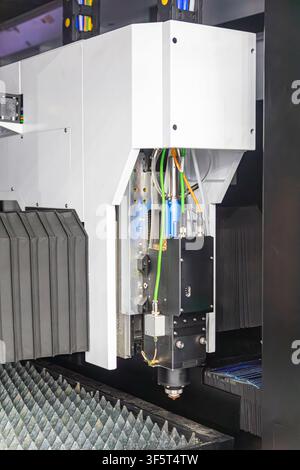 Industrial fiber laser cutting machine head positioned over a metal slatted worktable. High-precision automated CNC equipment for sheet metal fabricat Stock Photo