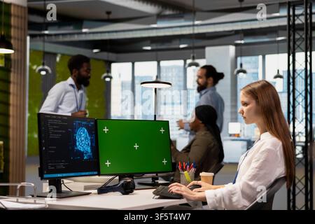 Junior developer using mockup PC, writing code, developing machine learning APIs. Young technician in office troubleshooting software errors using artificial intelligence tech on green screen computer Stock Photo