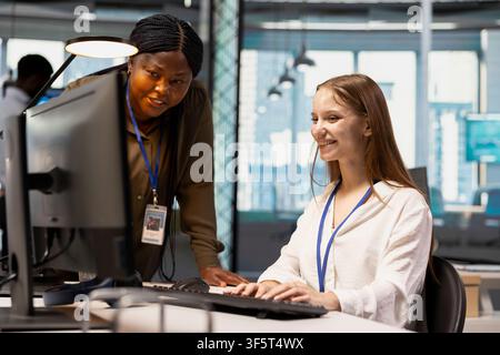 Friendly IT team leader teaching young software developer to use artificial intelligence. Joyous supervisor guiding junior dev through AI tool integration, mentoring her on using deep learning APIs Stock Photo