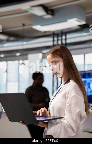Young female technician using laptop, designing and developing software applications, optimizing code for performance and scalability. Intern in office using notebook to resolve bottlenecks Stock Photo