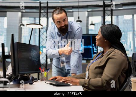 Pleased tech company manager doing thumbs up hand gesture, pleased by female developer managing to optimize code. Satisfied supervisor offering positive feedback to tasks solved by worker Stock Photo