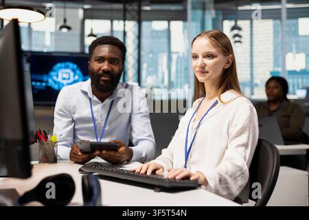 IT staff member helping female developer coding during internship in AI tech startup. Man providing support to new worker using computer in artificial intelligence agency Stock Photo