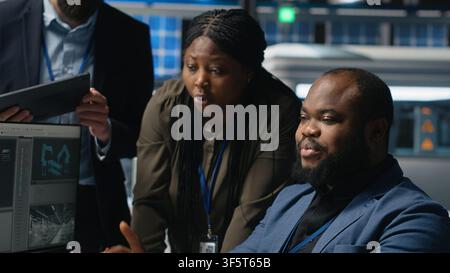 Group of professional consultants reviewing data and checklists in a high tech solar panel plant, ensuring manufacturing process meets sustainable energy and innovation standards. Camera B. Stock Photo