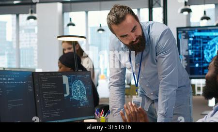 Manager supervising developer with paraplegia writing code, developing deep learning APIs. Supervisor overseeing work done by IT expert in wheelchair troubleshooting software errors using AI, camera A Stock Photo