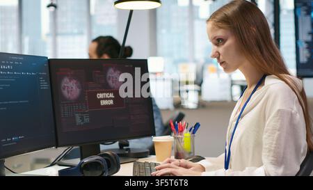Female programmer in startup office struggling to fix application errors while coding. Young woman dealing with computer bugs while coding in software development agency, camera A Stock Photo