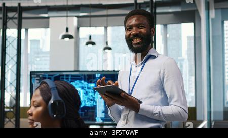 Happy programmer designing and developing software applications, optimizing code for performance and scalability. Joyous IT expert in office using tablet to resolving bottlenecks, camera A Stock Photo