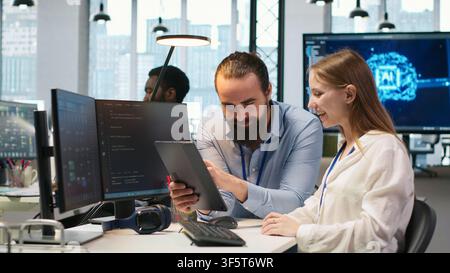 Friendly team leader helping happy young engineer code AI algorithms to debug software issues and improving system stability. Helpful manager assisting smiling intern in tech startup office, camera A Stock Photo