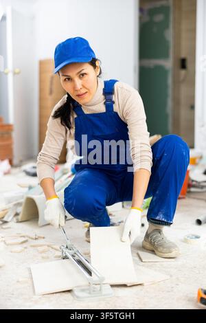 Woman builder cuts ceramic tiles with tile cutter Stock Photo
