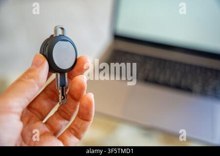 Hand holding an RFID key fob in front of a computer monitor. Concept of programming electronic access credentials, smart security systems and digital Stock Photo