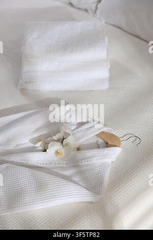 Clean bathrobe, towels and flowers on bed indoors, closeup Stock Photo