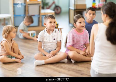 Kindergarten teacher reading to children in kindergarten. Children listen attentively to lessons, engaged in learning activities together Stock Photo