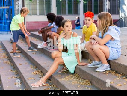 Happy tweenagers friends sitting on steps outdoors and chatting Stock Photo
