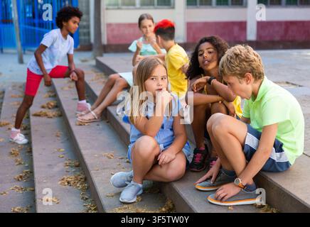 Positive tweenagers friendly blabbing while sitting on steps outdoors Stock Photo