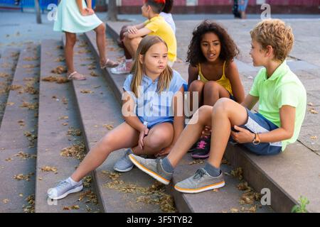 Happy tweenagers friends sitting on steps outdoors and chatting Stock Photo