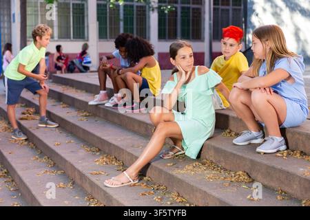 Happy tweenagers friends sitting on steps outdoors and chatting Stock Photo