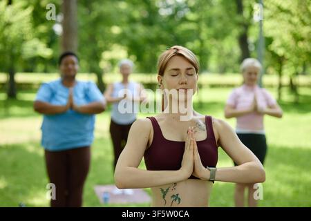 Woman Practicing Yoga with Diverse Group in Park Stock Photo