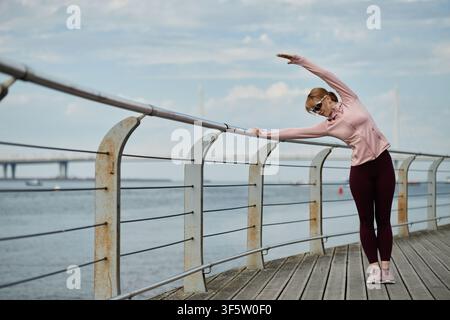 Woman Doing Side Bend Stretch on Waterfront Boardwalk Stock Photo