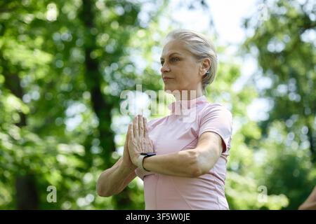 Middle Aged Woman Practicing Yoga and Meditating in Summer Park Stock Photo
