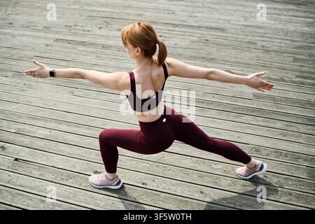 Woman Practicing Warrior Yoga Pose on Wooden Terrace Outdoors Stock Photo
