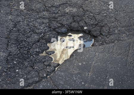 Water reflects on a cracked street surface Stock Photo